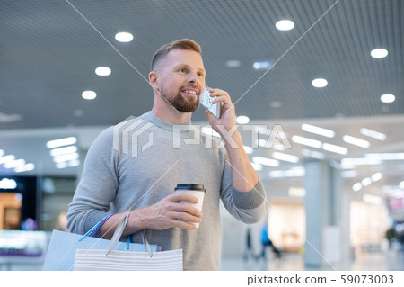 Young man with smartphone, drink and paperbags calling online shop Young man with smartphone, drink and paperbags calling online shop 59073003