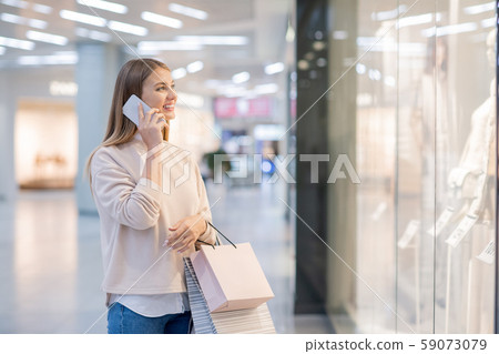 Young woman with paperbags talking to someone on mobile phone by shopwindow Young woman with paperbags talking to someone on mobile phone by shopwindow 59073079