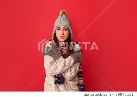 Freestyle. Young woman wearing scarf and hat standing isolated on red hugging herself feeling cold Freestyle. Young woman wearing scarf and hat standing isolated on red hugging herself feeling cold 59073181