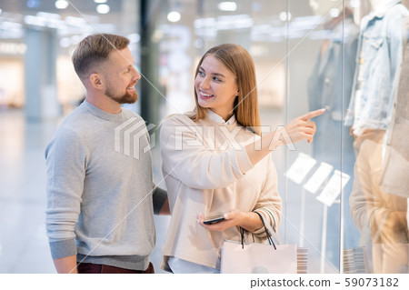 Young woman pointing at coat in shop window while looking at her husband 59073182