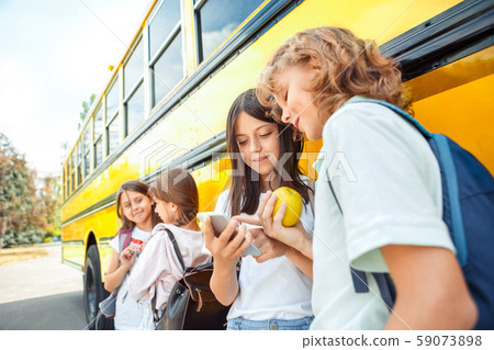Classmates going to school by bus standing talking eating apple browsing smartphone smiling curious Classmates going to school by bus standing talking eating apple browsing smartphone smiling curious 59073898