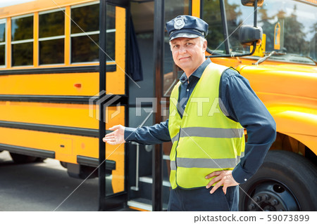Senior driver standing near school bus showing door smiling friendly Senior driver standing near school bus showing door smiling friendly 59073899