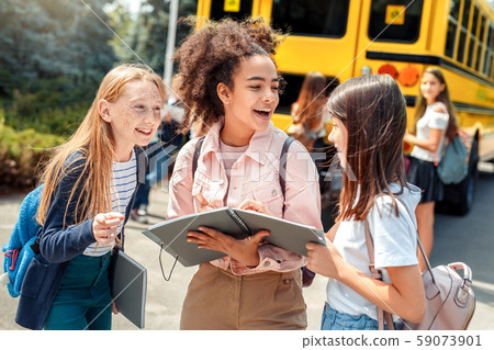 Classmates going to school by bus girls standing close-up reading notebook discussing assignment Classmates going to school by bus girls standing close-up reading notebook discussing assignment 59073901