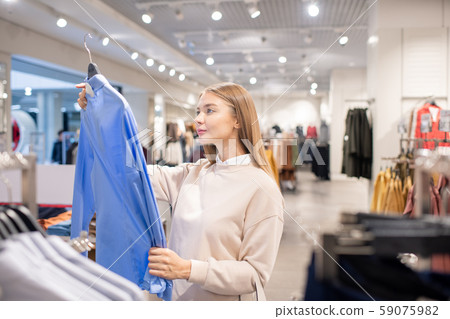 Casual blonde woman looking at blue shirt in clothing department 59075982