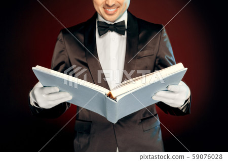 Professional Occupation. Magician in suit and gloves standing isolated on wall reading magic book Professional Occupation. Magician in suit and gloves standing isolated on wall reading magic book 59076028