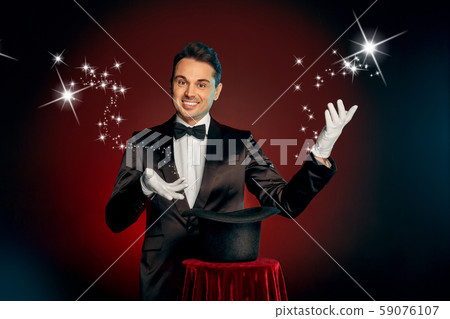 Professional Occupation. Magician in suit and gloves standing isolated on wall making trick with hat 59076107