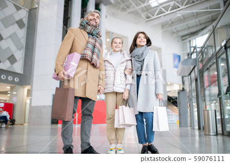 Young cheerful family of three in coats carrying paperbags 59076111