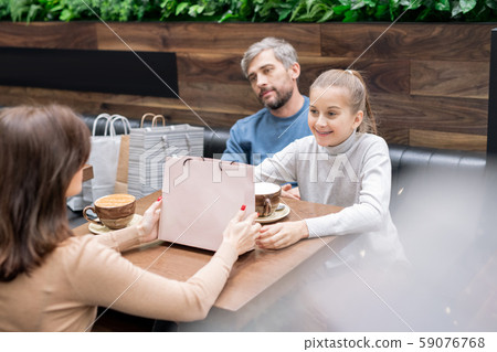 Pretty girl and her mother with paperbag looking at one another by table in cafe Pretty girl and her mother with paperbag looking at one another by table in cafe 59076768