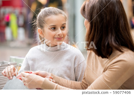 Pretty girl in white pullover looking at mom while discussing what they bought 59077406