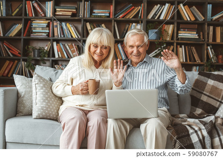 Senior couple together at home retirement concept sitting using laptop video call communication 59080767