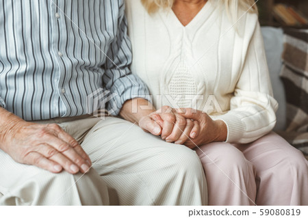Senior couple together at home retirement concept sitting holding hands close-up Senior couple together at home retirement concept sitting holding hands close-up 59080819