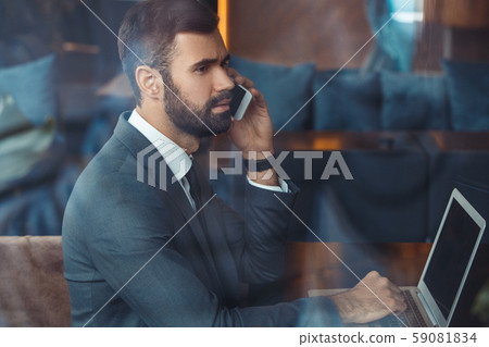 Businessman sitting in a business center restaurant with laptop phone call Businessman sitting in a business center restaurant with laptop phone call 59081834