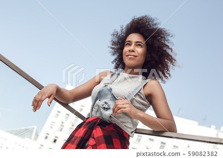 Young woman in the city standing on balcony leaning on fence looking aside dreaming joyful 59082382