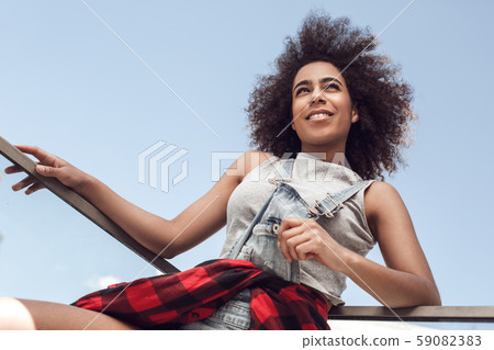 Young woman in the city standing on balcony leaning on fence looking aside playful bottom view 59082383