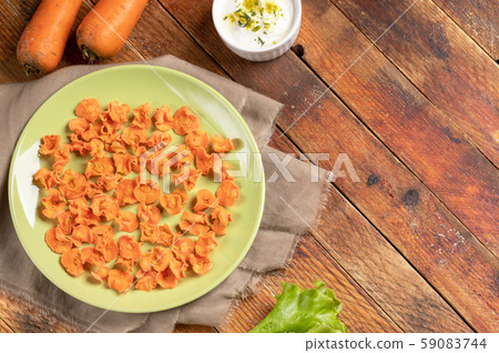 Healthy homemade carrot chips on round green plate, cup with sour cream sauce, whole carrots on fabric on rustic wooden background. Natural healthy vegetable snack. Alternative to ready-made chips. Healthy homemade carrot chips on round green plate, cup with sour cream sauce, whole carrots on fabric on rustic wooden background. Natural healthy vegetable snack. Alternative to ready-made chips. 59083744