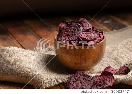 Homemade beetroot chips in wooden bowl on burlap on old wooden table on dark background. Natural healthy vegetable snack. Alternative to ready-made chips. Copy space. Homemade beetroot chips in wooden bowl on burlap on old wooden table on dark background. Natural healthy vegetable snack. Alternative to ready-made chips. Copy space. 59083747
