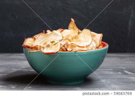 Close-up one turquoise ceramic bowl with healthy homemade apple chips on dark grey background. Low key. Fruit healthy snack. Selective focus. 59083769