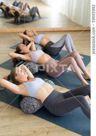 Restorative yoga with a bolster. Group of three young sporty attractive women in yoga studio, lying Restorative yoga with a bolster. Group of three young sporty attractive women in yoga studio, lying 59085992
