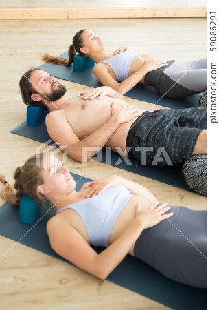 Restorative yoga with a bolster. Group of young sporty attractive people in yoga studio, lying on Restorative yoga with a bolster. Group of young sporty attractive people in yoga studio, lying on 59086291