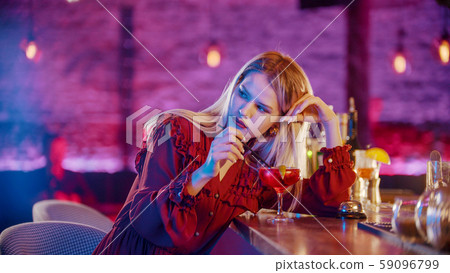 Gorgeous bored young woman sitting by the bartender stand and stirs the drink with a straw and 59096799