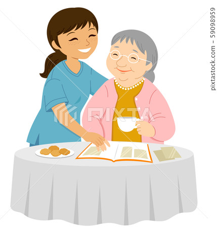 Young female caregiver smiling to an elderly woman who is placing photos in an album Young female caregiver smiling to an elderly woman who is placing photos in an album 59098959