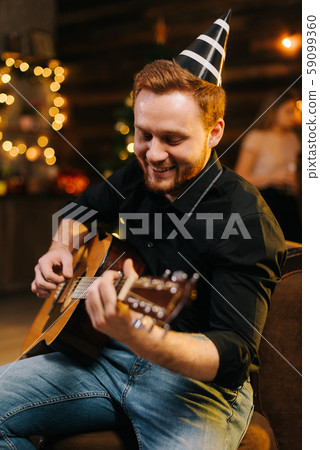 Portrait of young cheerful man in the festive hat playing on the guitar. Portrait of young cheerful man in the festive hat playing on the guitar. 59099360