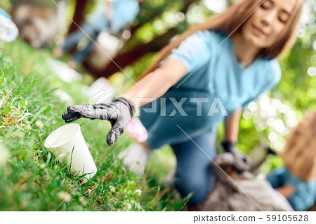 Volunteering. Young people volunteers outdoors girl close-up picking plastic cup blurred background 59105628