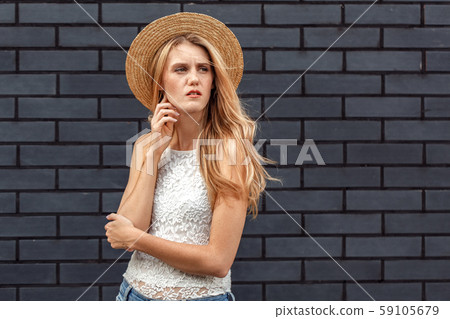 Windy Weather. Young woman in hat standing isolated on wall looking aside concerned Windy Weather. Young woman in hat standing isolated on wall looking aside concerned 59105679
