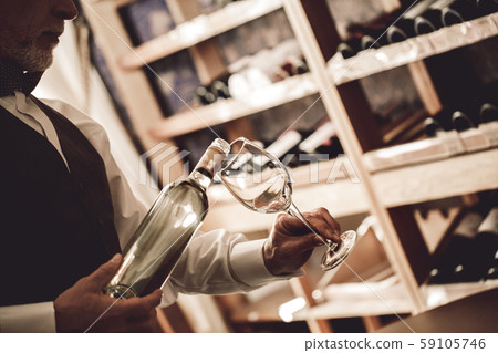 Sommelier Concept. Senior man standing pouring white wine into glass concentrated close-up Sommelier Concept. Senior man standing pouring white wine into glass concentrated close-up 59105746