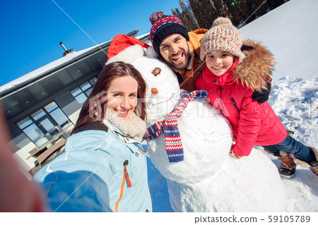 Winter vacation. Family time together outdoors standing near house taking selfie with snowman Winter vacation. Family time together outdoors standing near house taking selfie with snowman 59105789
