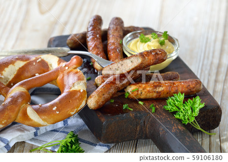 Fried Bavarian sausages from Nuremberg with mustard and pretzel served on a rustic steak board Fried Bavarian sausages from Nuremberg with mustard and pretzel served on a rustic steak board 59106180