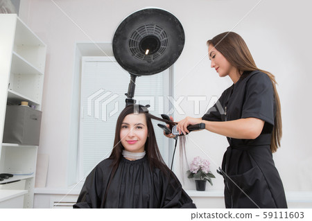 Attractive brunette hairdresser thoroughly dyeing hair of female client while she is sitting in 59111603
