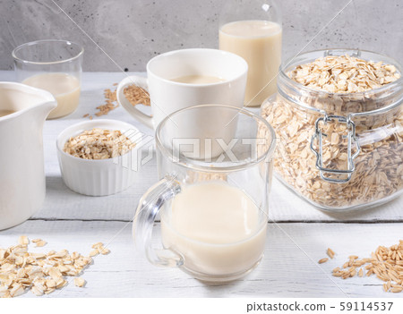 Close-up set of different glasses and bottle with healthy dairy free oat milk, jar with oat flakes on white painted wooden table near grey concrete wall. Best lactose free substitutes of milk concept. Close-up set of different glasses and bottle with healthy dairy free oat milk, jar with oat flakes on white painted wooden table near grey concrete wall. Best lactose free substitutes of milk concept. 59114537