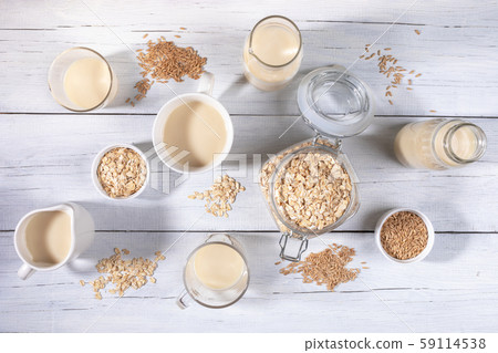 Set of different glass containers with healthy dairy free oat milk, oat seeds and flakes on white painted wooden table. Best lactose free substitutes of milk concept. Top view, flat lay. Set of different glass containers with healthy dairy free oat milk, oat seeds and flakes on white painted wooden table. Best lactose free substitutes of milk concept. Top view, flat lay. 59114538
