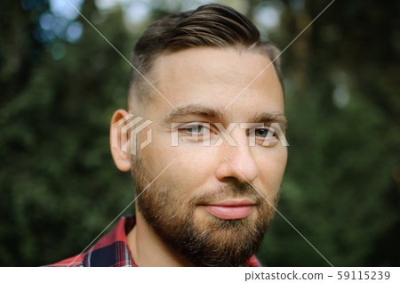 Close up portrait of young bearded man in red shirt looking at the camera with smile in the park on 59115239