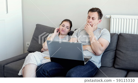 Bored sleepy couple man and woman are watching video on laptop sitting on sofa.