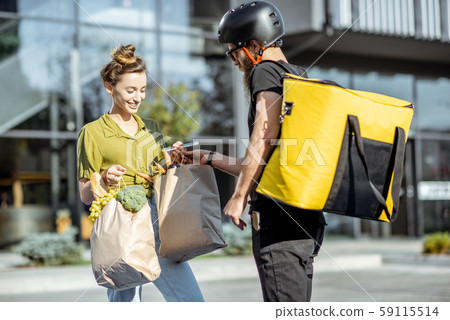 Courier delivering groceries to a young woman outdoors 59115514