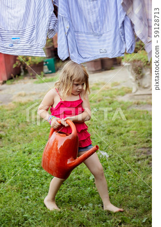 Little girl in the backyard, carrying bucket full 59128713