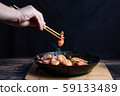 Chef at work. Hand holds a chopsticks under hot pan with fried vegetables, broccoli, cauliflower, carrots and shrimp. Process of preparation of vegetables over dark background 59133489