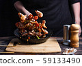 Chef at work. Hand holds a hot pan with fried shrimp and vegetables in sweet and sour sauce. Process of preparation of shrimps over dark background 59133490