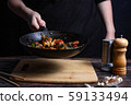 Chef at work. Hand holds a hot pan with fried vegetables, broccoli, cauliflower, carrots. Process of preparation of vegetables over dark background 59133494