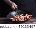 Chef at work. Hand holds a hot pan with fried shrimp. Process of preparation of shrimps over dark background 59133497