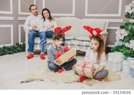 Full-body photo of cute children sitting in lotos position with a Christmas present in hands Full-body photo of cute children sitting in lotos position with a Christmas present in hands 59134036