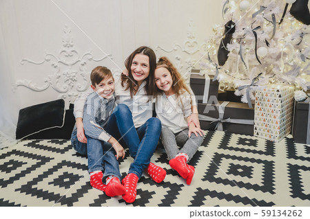 Little girl and boy with their mother are sitting on the vintage carpet near fir-tree, enjoying time 59134262