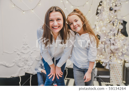Cheerful mother and daughter near beautiful decorated Christmas tree, leaning to the camera. Cheerful mother and daughter near beautiful decorated Christmas tree, leaning to the camera. 59134264
