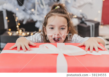 Closeup photo of super excited young girl opening large christmas present while sitting on living 59134555