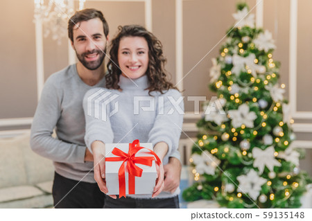 Defocused man and woman holding a present tied with a red ribbon, looking at the camera smilling. Defocused man and woman holding a present tied with a red ribbon, looking at the camera smilling. 59135148