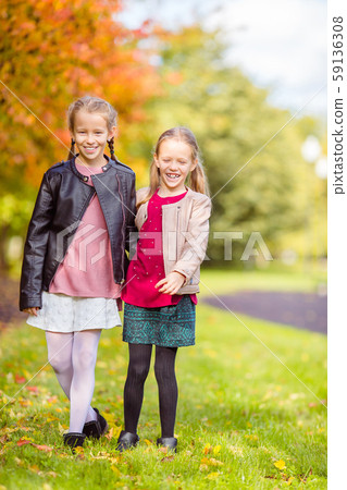 Little adorable girls at warm day in autumn park outdoors Little adorable girls at warm day in autumn park outdoors 59136308