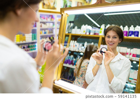 Young beautiful girl chooses her tone cream or powder and picks up on skin tone in front of big Young beautiful girl chooses her tone cream or powder and picks up on skin tone in front of big 59141135