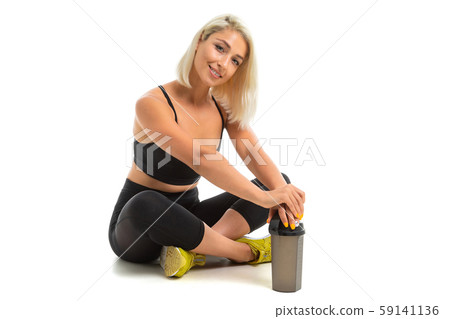 Sport caucasian girl sits on a floor in sport wear and keep a bottle with water in her hands Sport caucasian girl sits on a floor in sport wear and keep a bottle with water in her hands 59141136